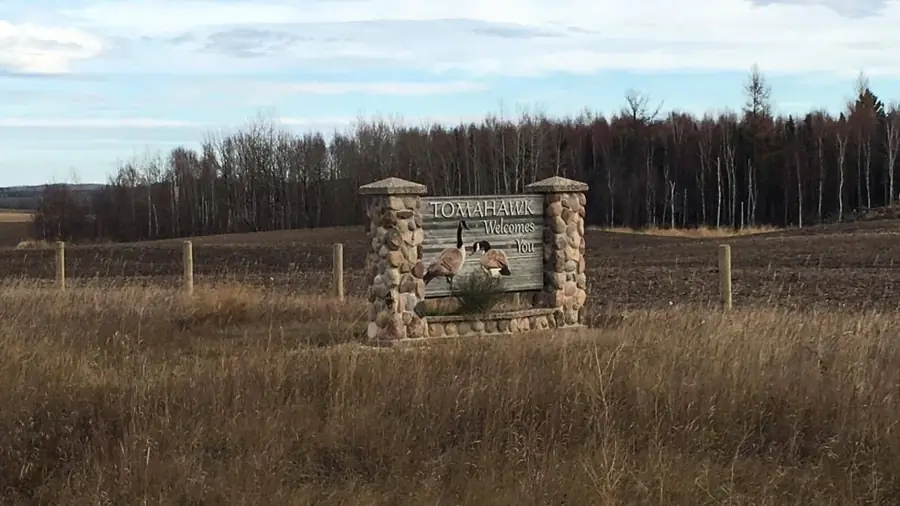 The stone Welcome to Tomahawk sign beside a field